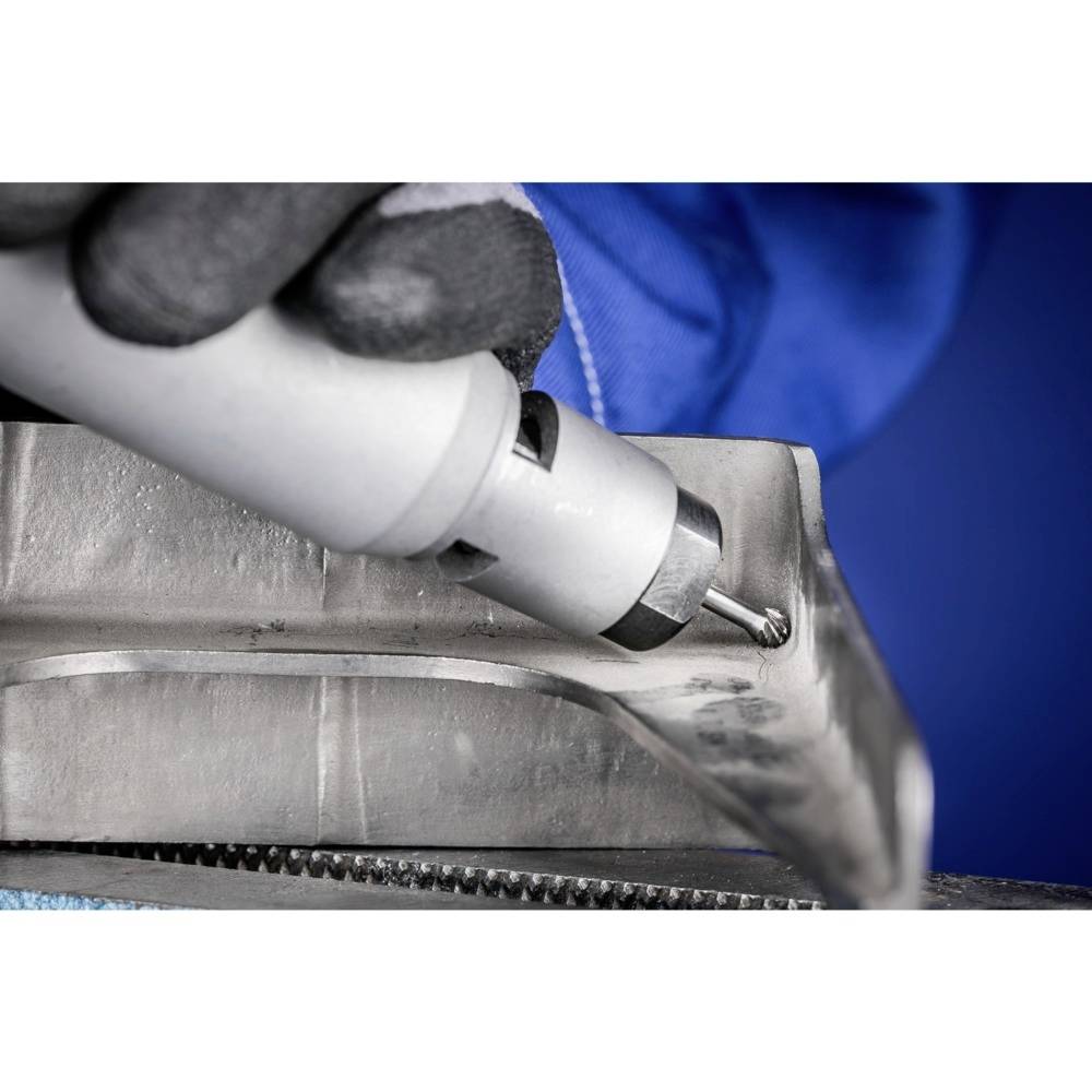 Zbliżenie pracownika w niebieskich rękawiczkach obrabiającego metal narzędziem. Koncentracja na precyzyjnej pracy.