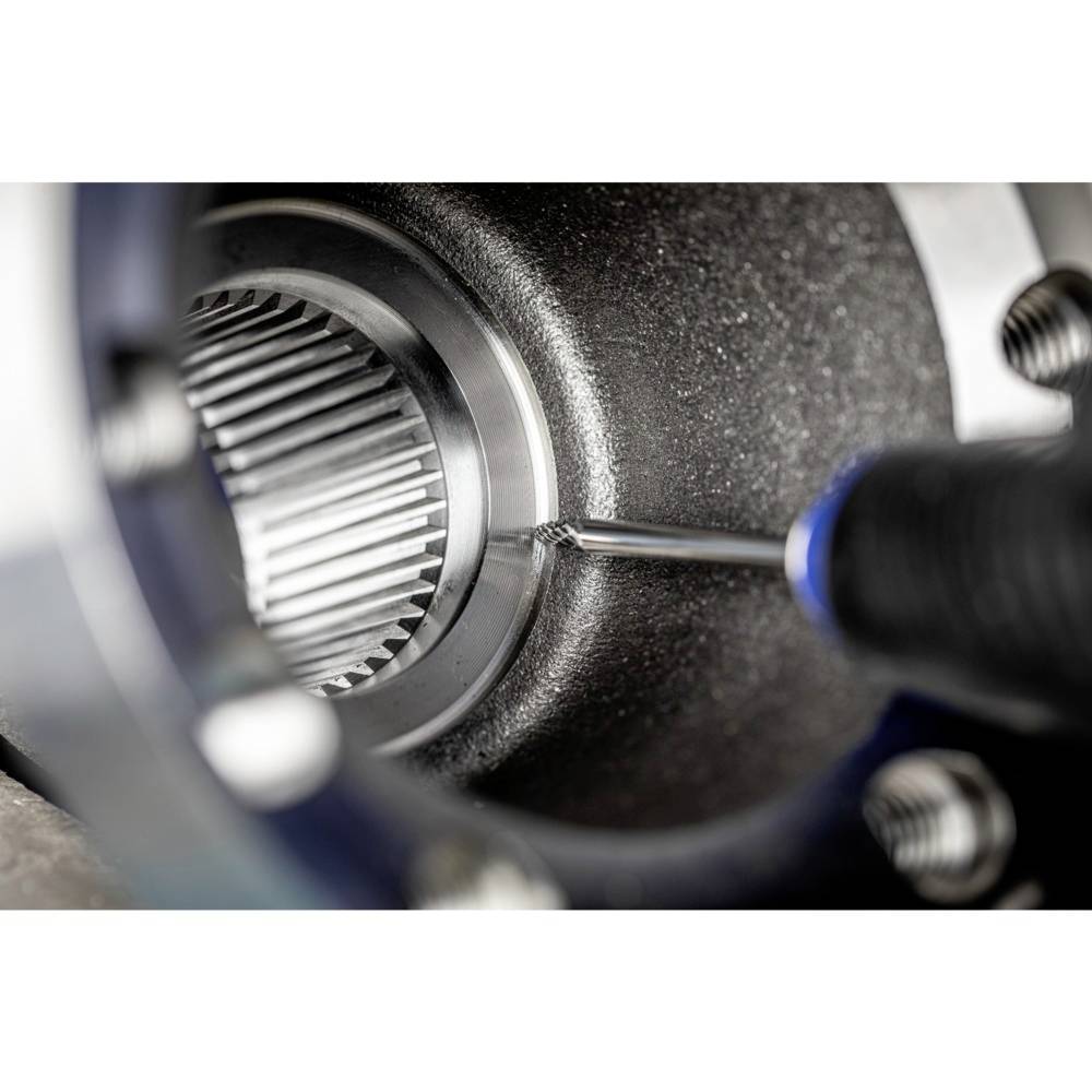 Zbliżenie metalowego koła zębatego montowanego wkrętakiem. Widoczne są szczegóły mechaniki przemysłowej.