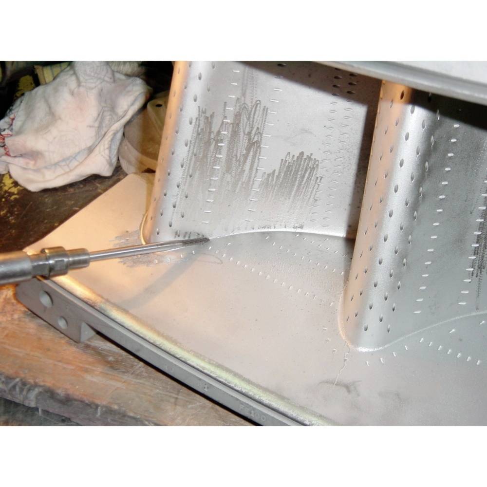 Zbliżenie metalowej powierzchni, z której usuwana jest skóra wiórowa. Narzędzie zostaje przyłożone do krawędzi.