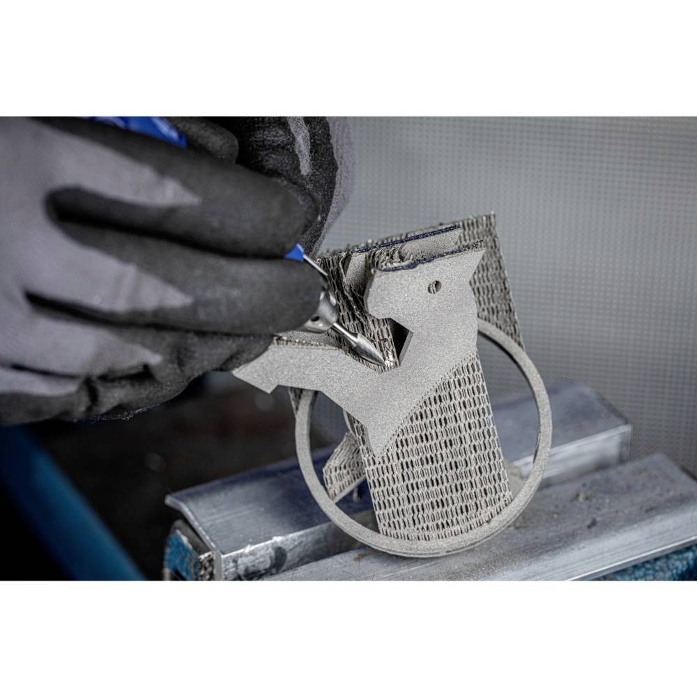 Ręka w rękawicy obrabia obiekt metalowy wydrukowany w technologii 3D na stole warsztatowym.