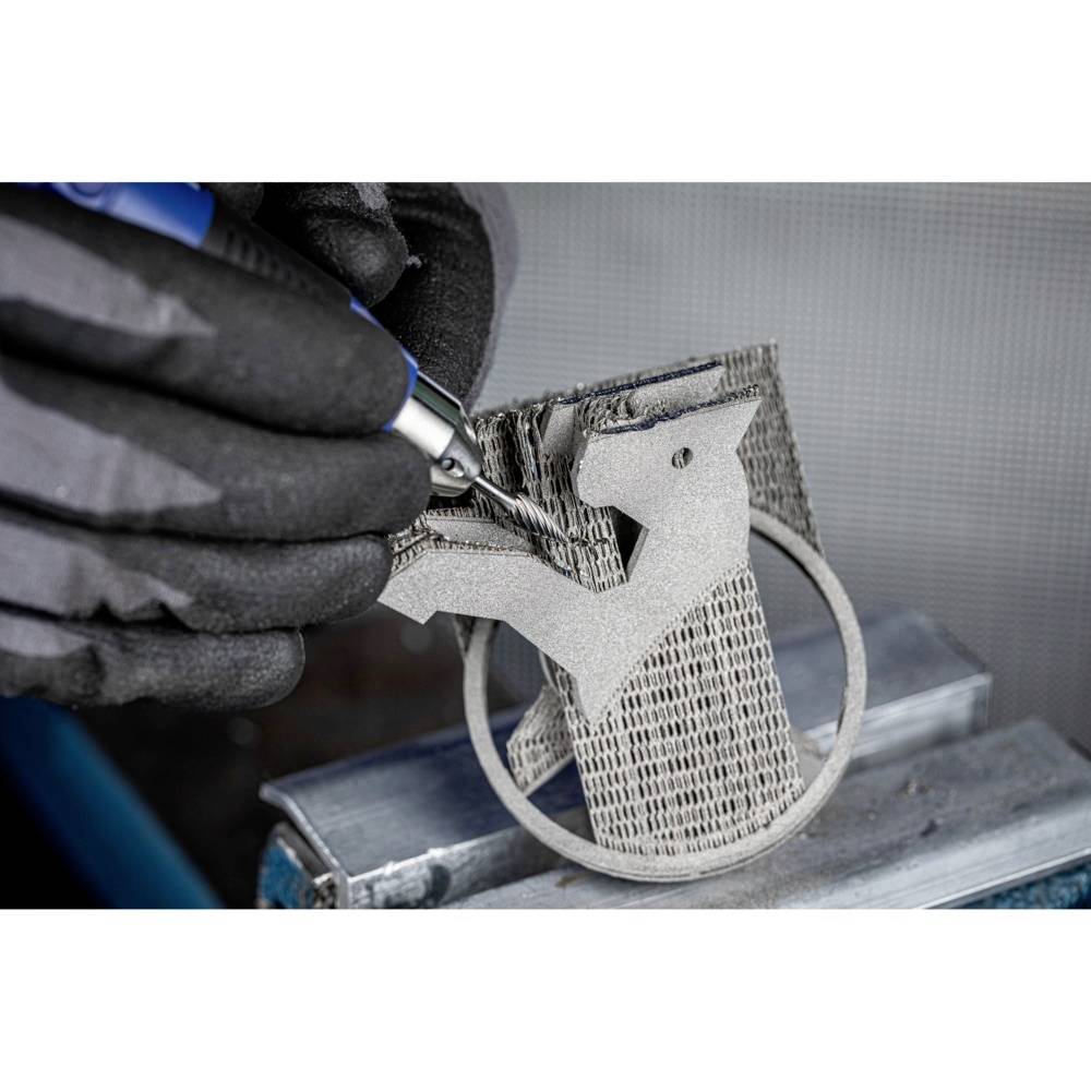 Dłoń w rękawicach roboczych obrabia trójwymiarową figurę metalową na stole warsztatowym przy użyciu narzędzia.