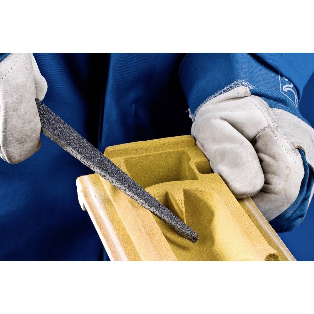 Osoba ostrożnie piluje kawałek drewna, prawdopodobnie element projektu stolarskiego. Jest ubrana w niebieskie ubranie i nosi rękawice ochronne.