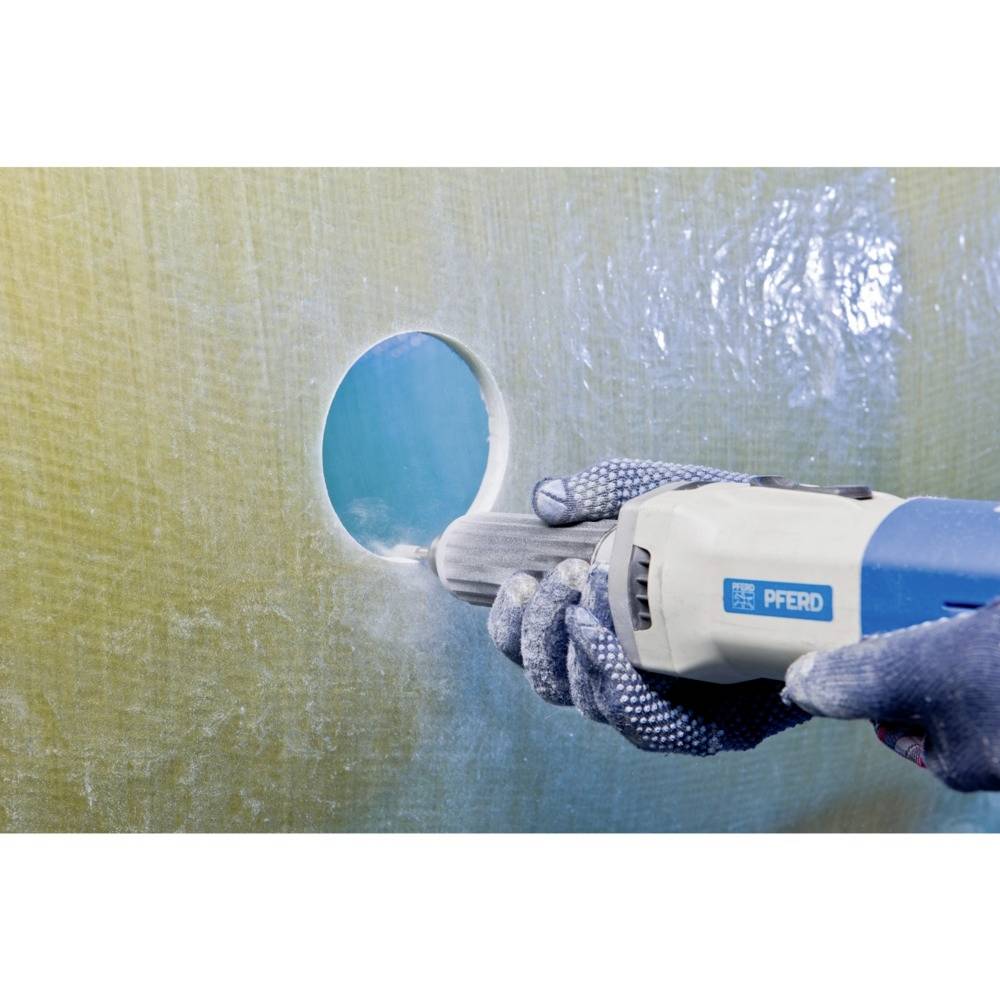 Osoba w rękawicach wycina okrągły otwór w gładkiej, błyszczącej powierzchni za pomocą elektronarzędzia.