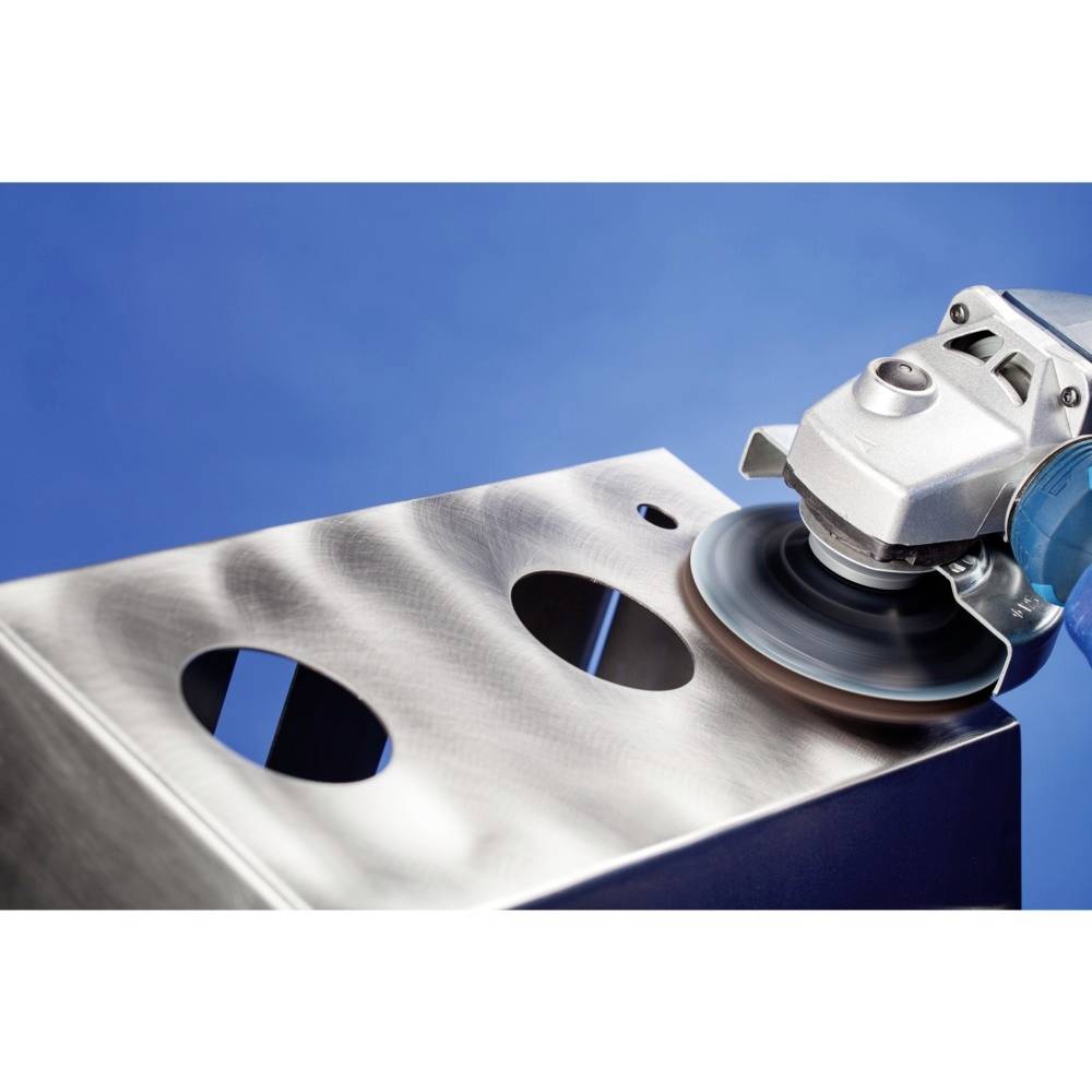 Szlifierka kątowa poleruje powierzchnię przetworzonego kawałka metalu z wywierczonymi otworami, na niebieskim tle.