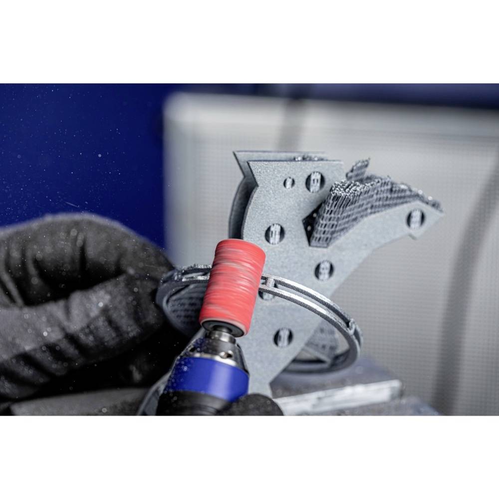 Osoba szlifuje metalową część wydrukowaną w technologii 3D za pomocą narzędzia obrotowego z czerwoną nasadką ścierną.