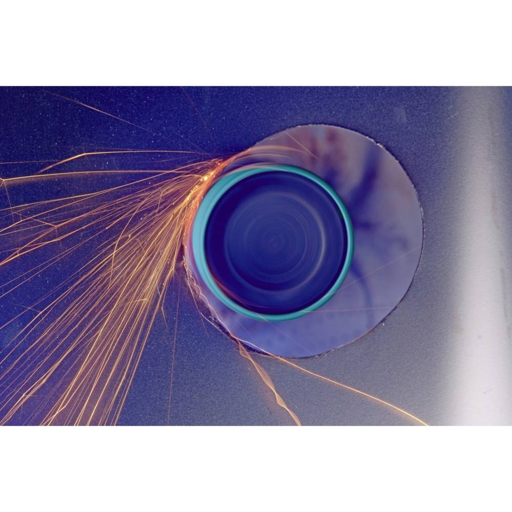 Wiertło wytwarza iskry i wycina otwór w powierzchni metalu. Główny nacisk położony jest na pojawiające się iskry i świecący otwór.