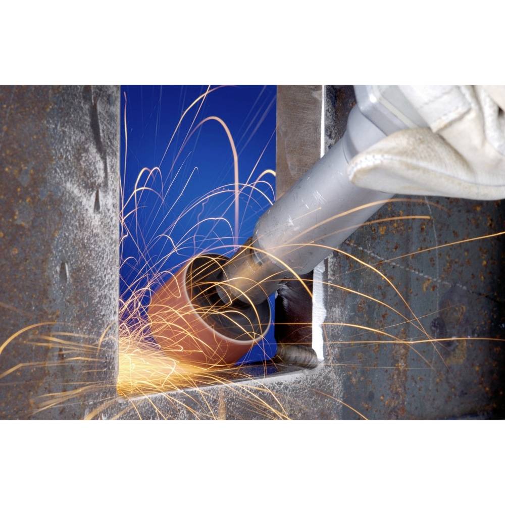 Osoba szlifuje metal szlifierką kątową. Iskry tryskają i świecą się na niebieskim tle.
