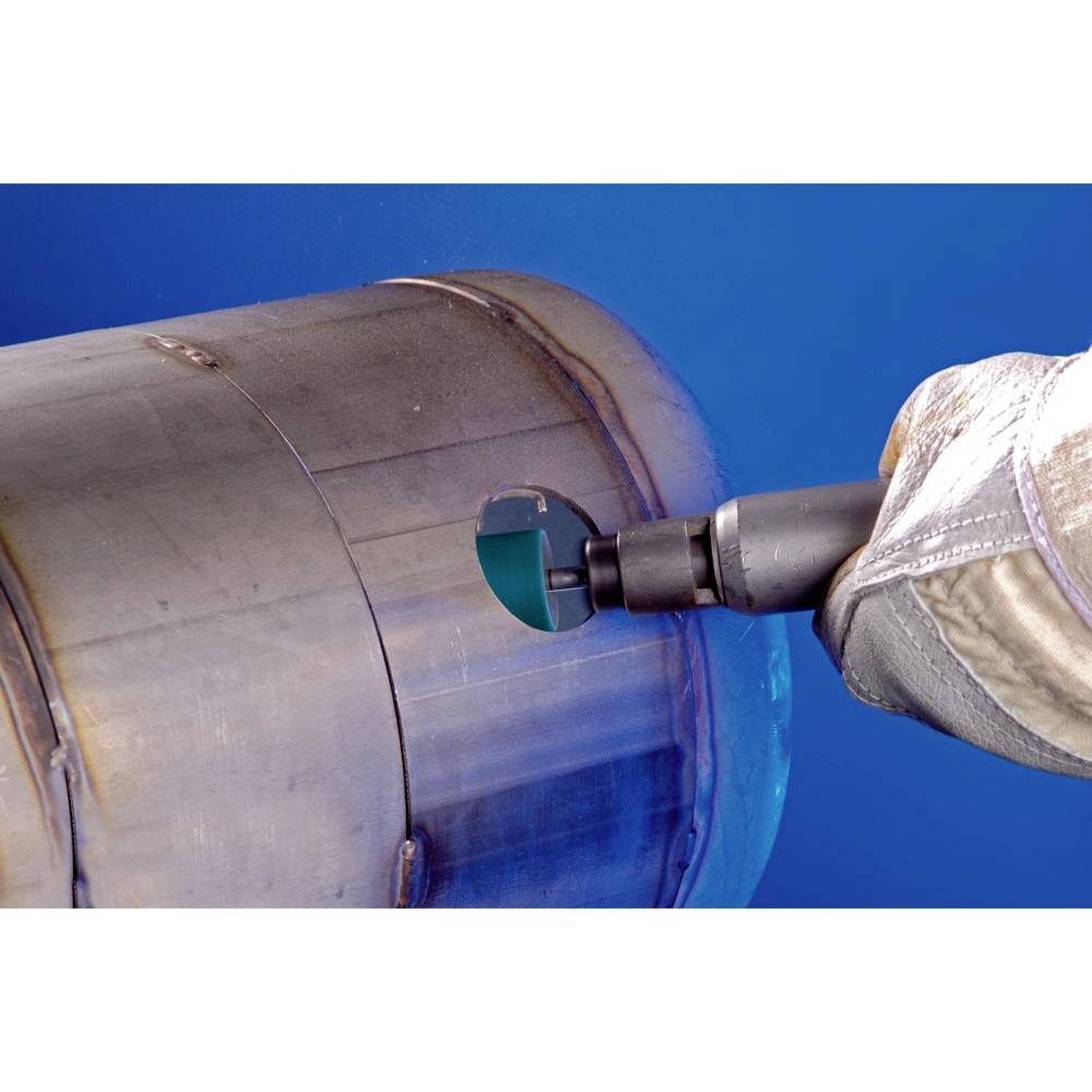 Duży metalowy cylinder z rękawicą przy wiertarce. Ręka precyzyjnie wierci okrągły otwór w powierzchni cylindra.