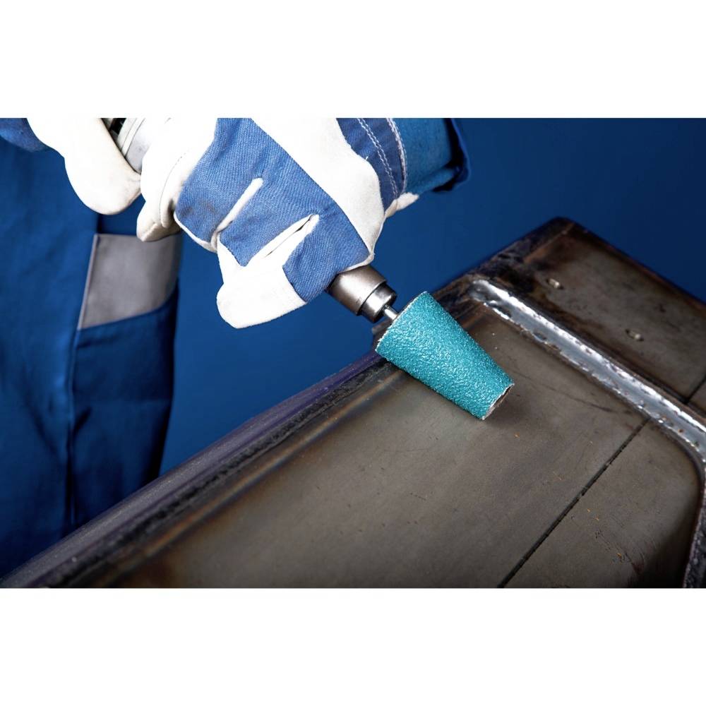 Osoba szlifuje powierzchnię metalową elektronarzędziem. Nosi niebieskie ubranie ochronne i białe rękawice.