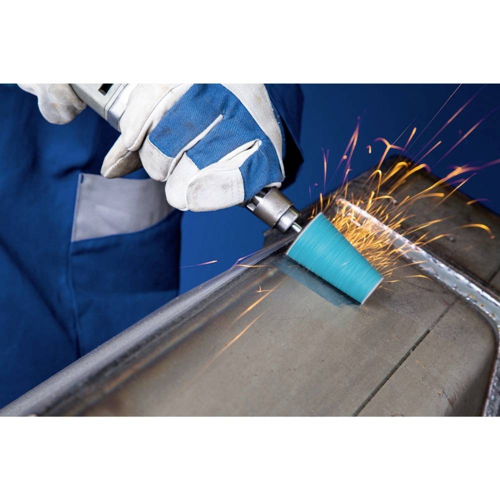 Osoba ubrana w niebieskie ubranie ochronne szlifuje metalową powierzchnię elektronarzędziem. Spod metalu lecą iskry.