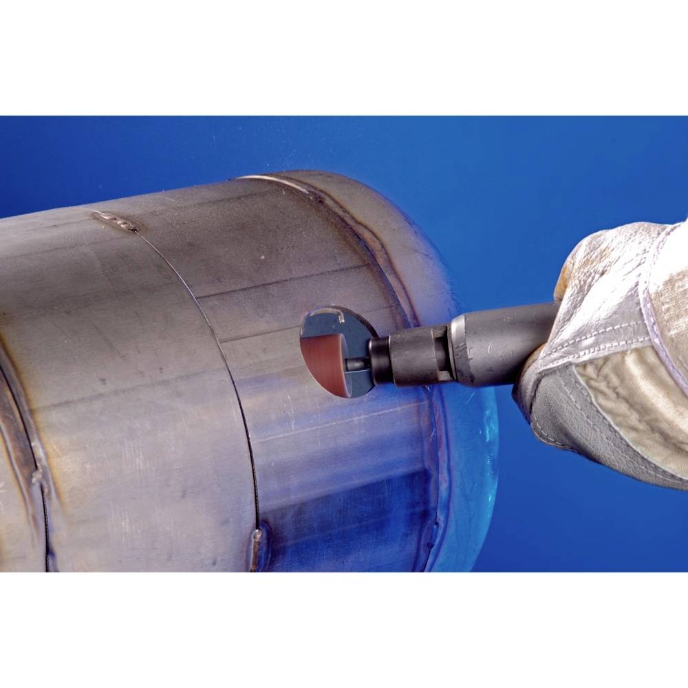 Dłoń w rękawicy roboczej trzyma narzędzie obrabiające metalowy cylinder. Tło jest niebieskie.