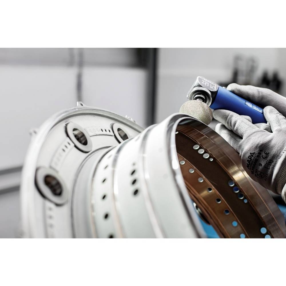 Osoba ubrana w rękawice robocze szlifuje niebieską szlifierką kątową metalowy obiekt z otworami.