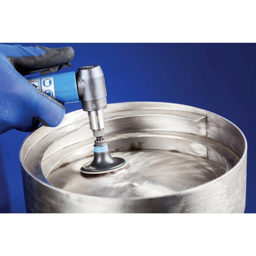 Osoba w niebieskich rękawiczkach poleruje metalowy cylinder ręcznym urządzeniem na niebieskim tle.