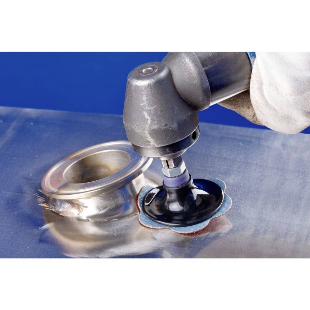 Jedna ręka trzyma elektryczne urządzenie szlifierskie i poleruje powierzchnię metalową. Obok leży okrągły obiekt metalowy.