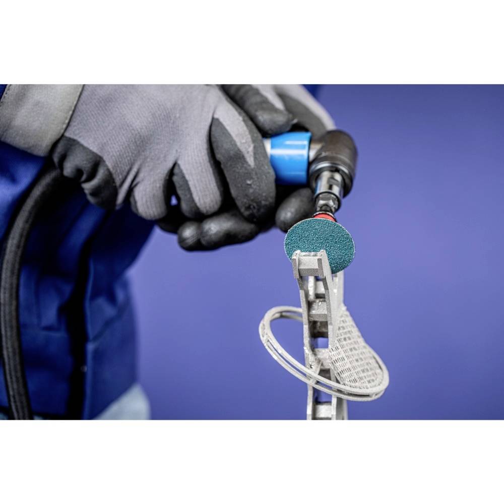 Osoba w szarych rękawiczkach i niebieskim ubraniu trzyma narzędzie szlifierskie, które obrabia metalowy przedmiot.