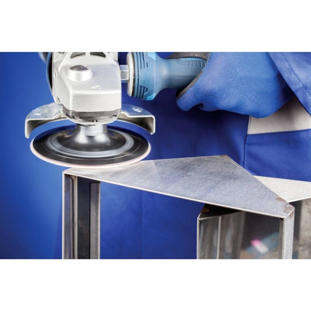 Robotnik szlifuje krawędź metalu szlifierką kątową. Fokus jest skierowany na wypolerowaną powierzchnię i narzędzie.