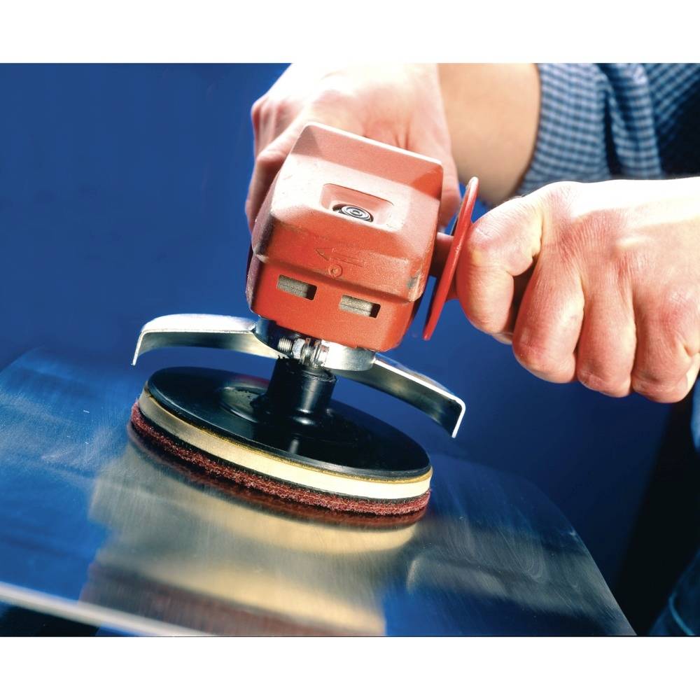 Osoba szlifuje metalową powierzchnię czerwonym elektronarzędziem. Ręce pewnie trzymają urządzenie.