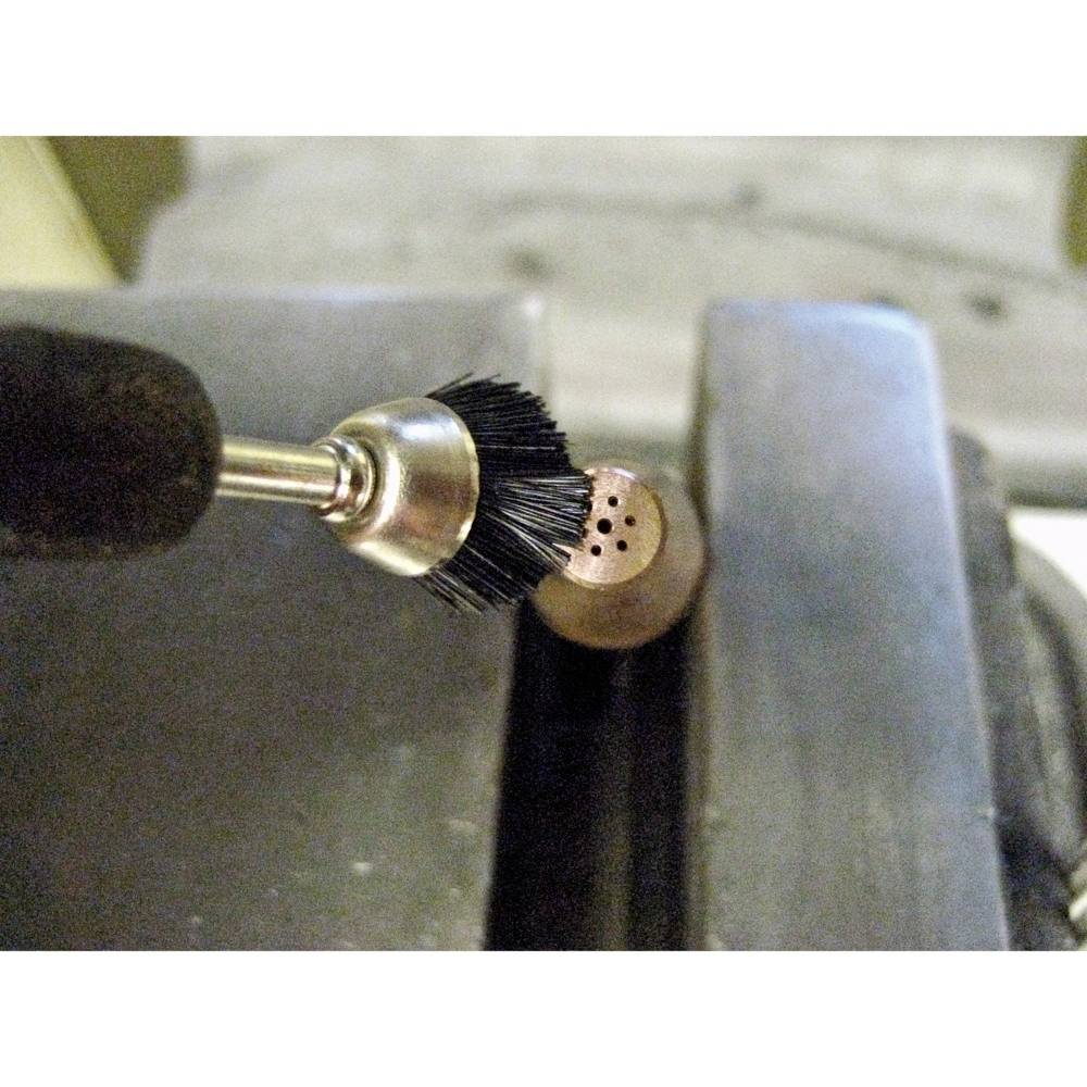 Obrotowe narzędzie z końcówką szczotkową poleruje powierzchnię kawałka miedzi zamocowanego w imadle.