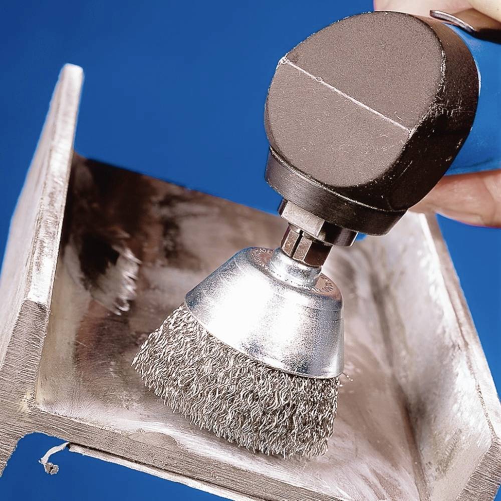 Szlifierka kątowa z drucianą szczotką poleruje metalową powierzchnię narożnika.