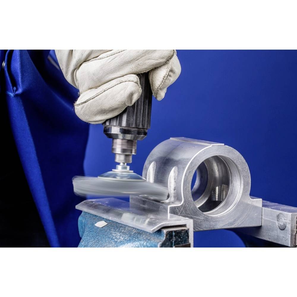 Dłoń w ochronnej rękawicy poleruje element metalowy szlifierką na niebieskim tle. Fokus na obsłudze narzędzia.