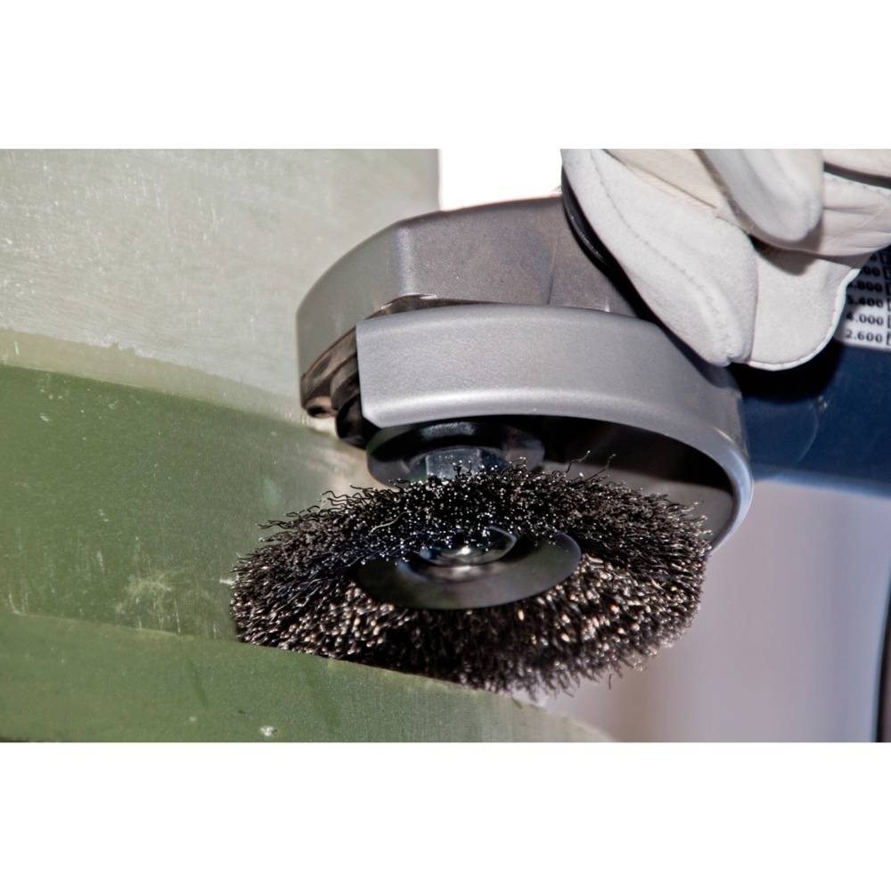 Zbliżenie szczotki drucianej w trakcie czyszczenia metalu za pomocą maszyny. Ręka w rękawicy mocno trzyma urządzenie.