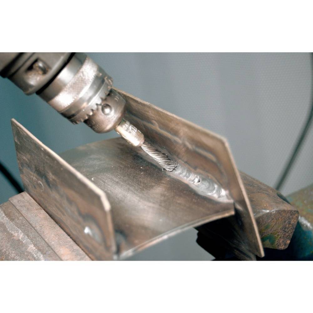 Wiertło metalowe obrabia dwie połączone ze sobą płyty metalowe. Płyty są zamocowane w imadle.