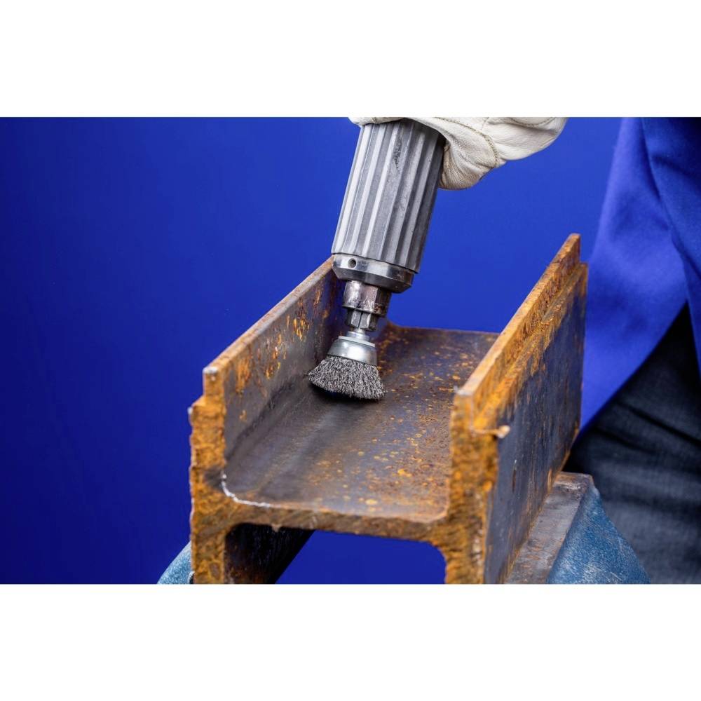 Osoba czyści szczotką drucianą rdzewiejące wnętrze profilu metalowego.