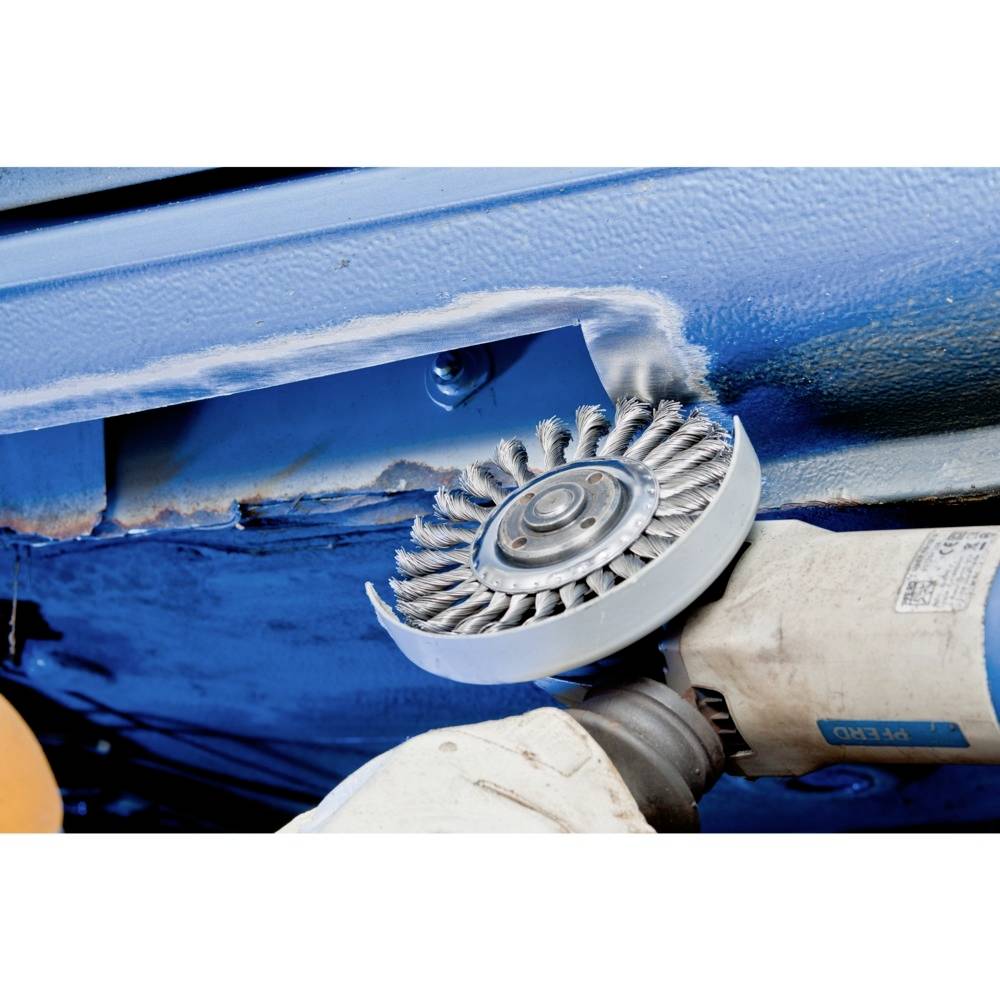 Szlifierka kątowa obrabia niebieskie metal, usuwając rdzę. Szczotka druciana sypie iskrami. Narzędzie jest trzymane przez jedną rękę.