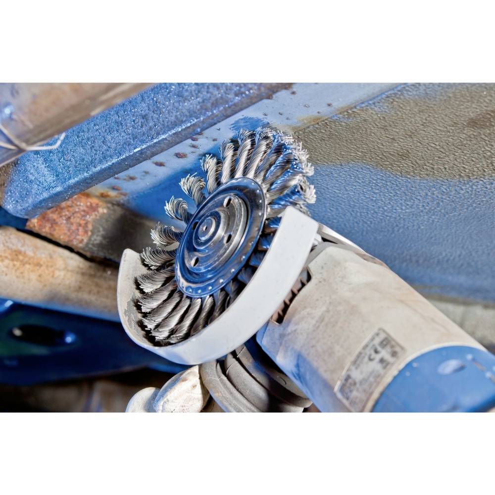 Szczotka druciana zamocowana w szlifierce kątowej usuwa rdzę z powierzchni metalowej w warunkach warsztatowych.