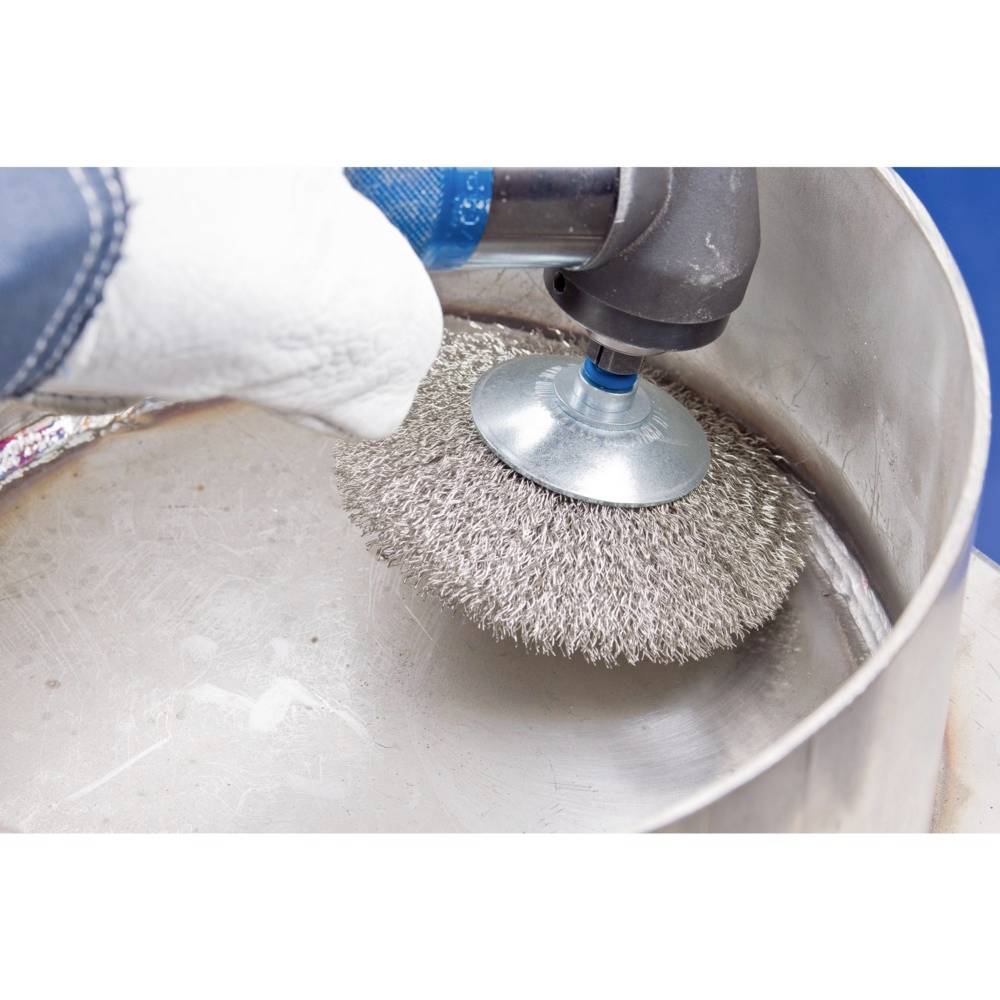 Ręka w rękawicy ochronnej trzyma obracające się narzędzie z druciną, czyszcząc wnętrze metalowego pojemnika.