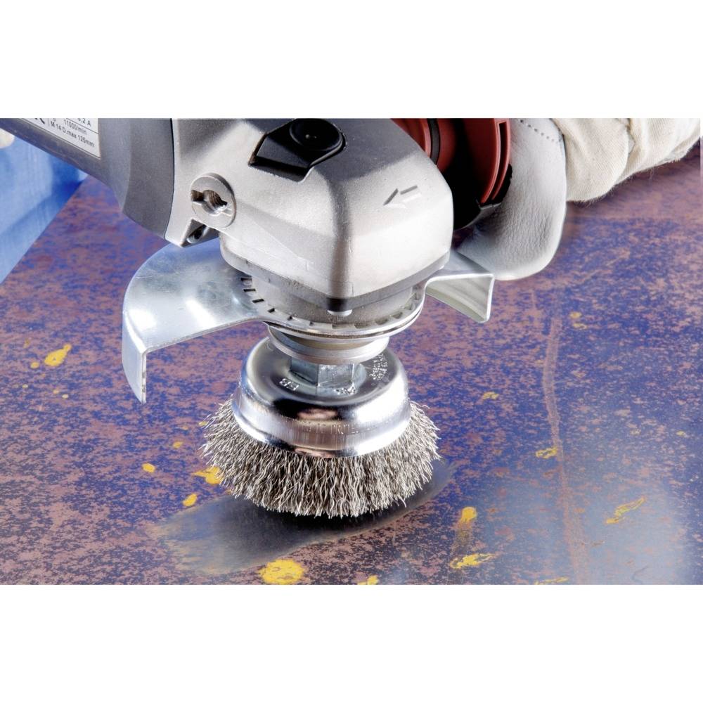 Szczotka druciana zamocowana na szlifierce kątowej czyści zardzewiałą powierzchnię metalową. Praca wymaga stosowania odzieży ochronnej.