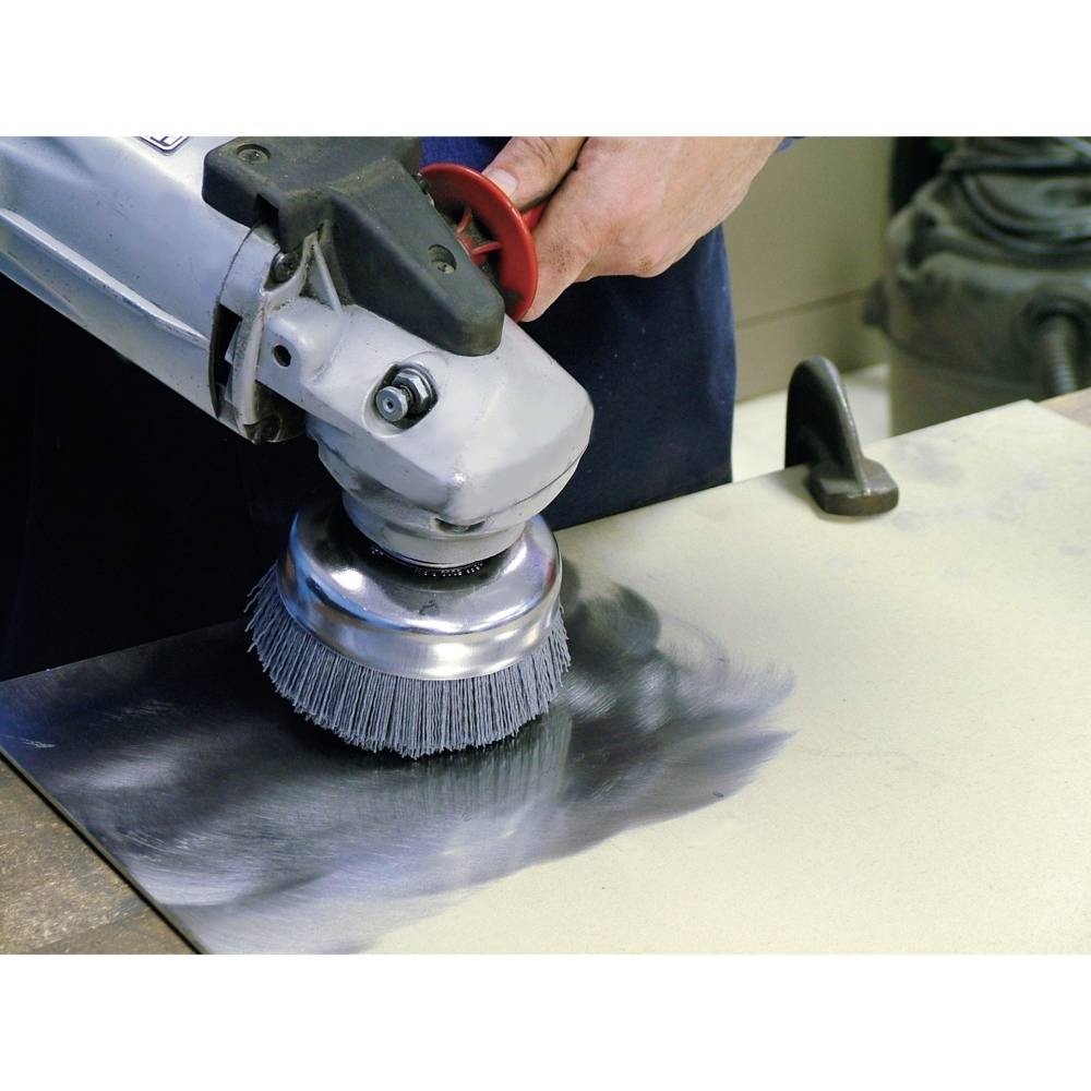 Osoba szlifuje metalową płytę obrotową szczotką, aby wygładzić lub wyczyścić jej powierzchnię.