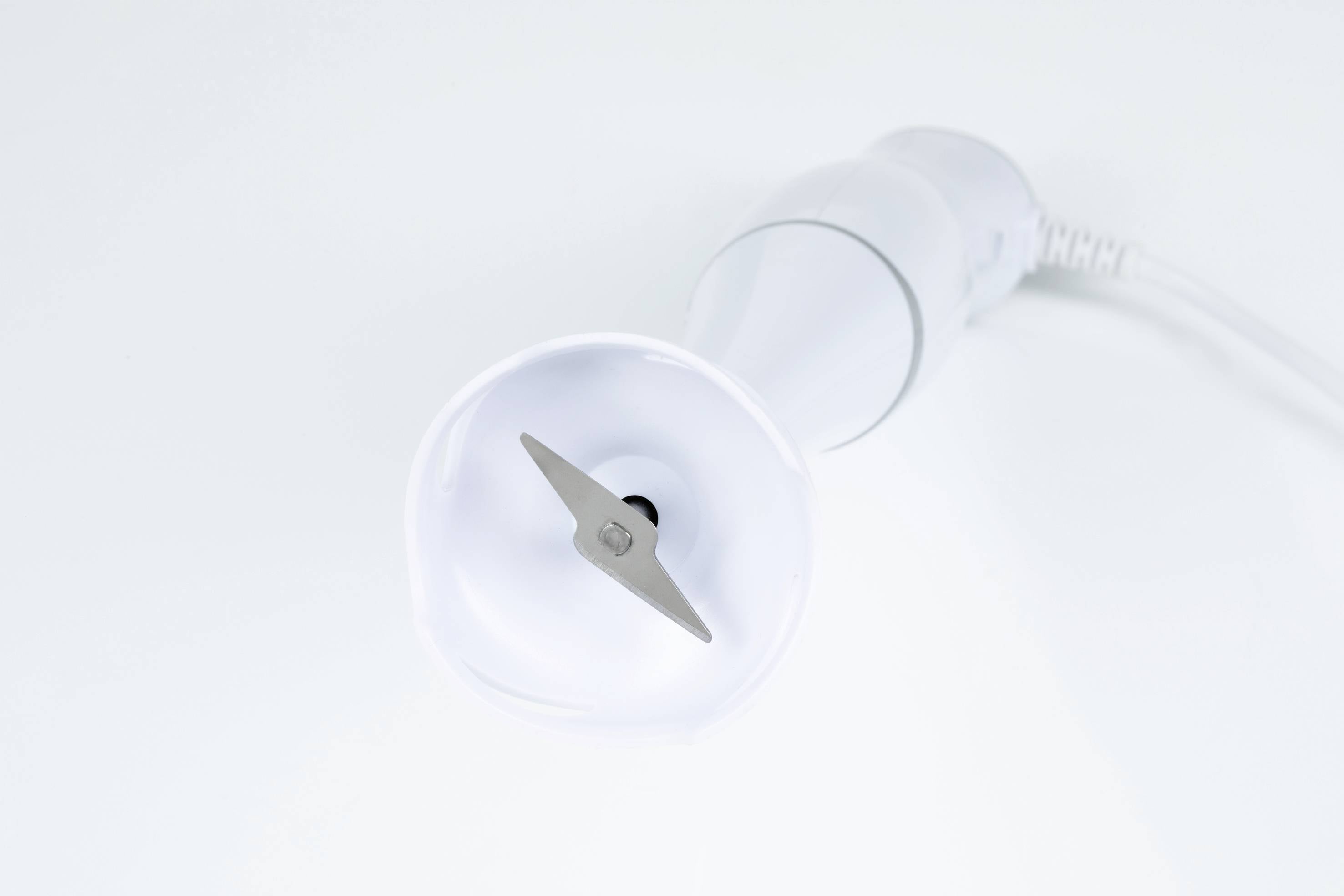 Biały blender ręczny widziany z góry z widocznym metalowym ostrzem, sfotografowany na białym tle.