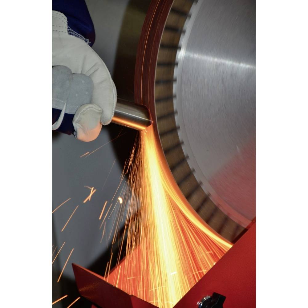 Osoba w odzieży ochronnej szlifuje metal szlifierką kątową, a wokół lecą iskry.