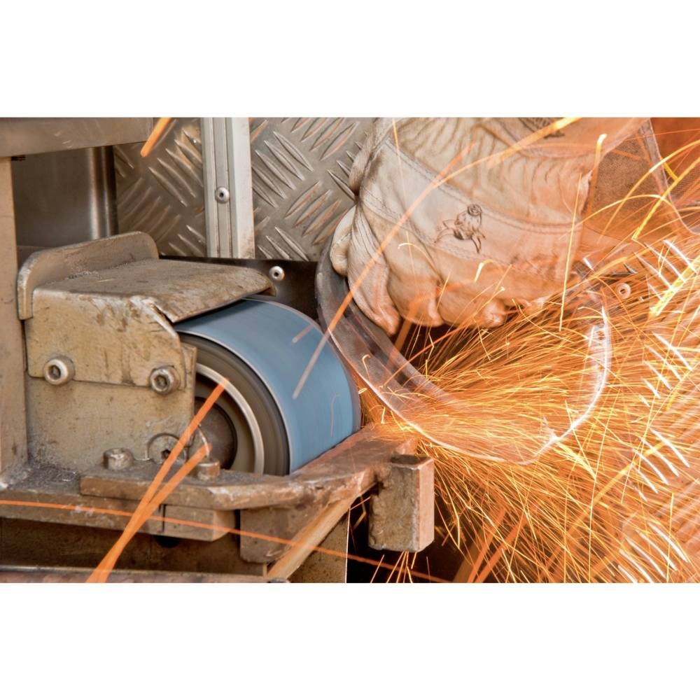 Ręka w rękawicy szlifuje element metalowy na urządzeniu szlifierskim. Od punktu kontaktu odpryskują iskry.