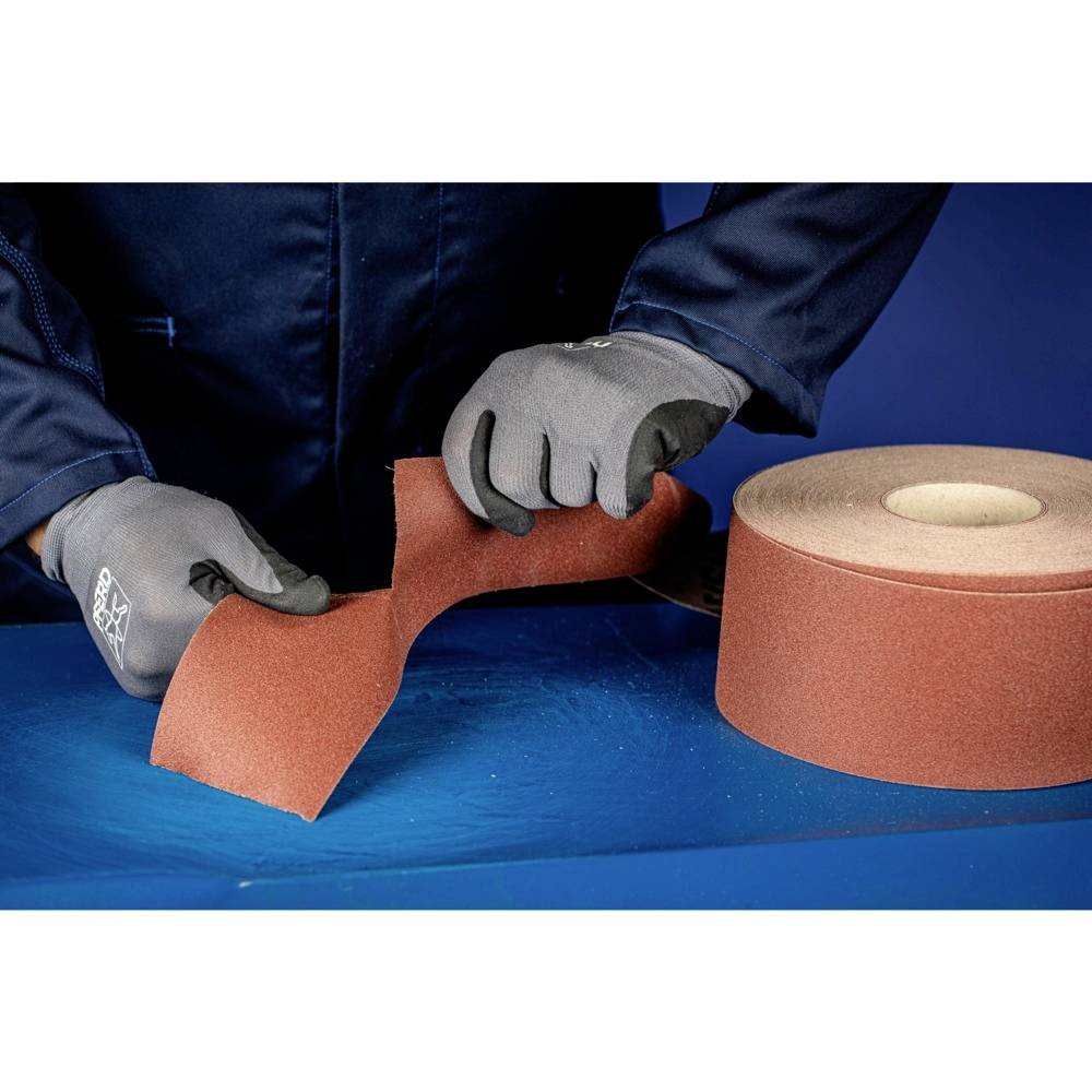 Osoba w szarych rękawiczkach odrywa kawałek czerwonego papieru ściernego z dużej rolki.