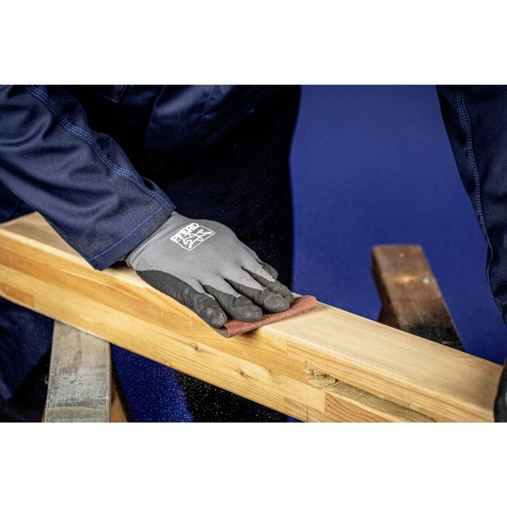 Osoba szlifuje kawałek drewna papierem ściernym, nosi rękawice robocze i niebieski kombinezon.