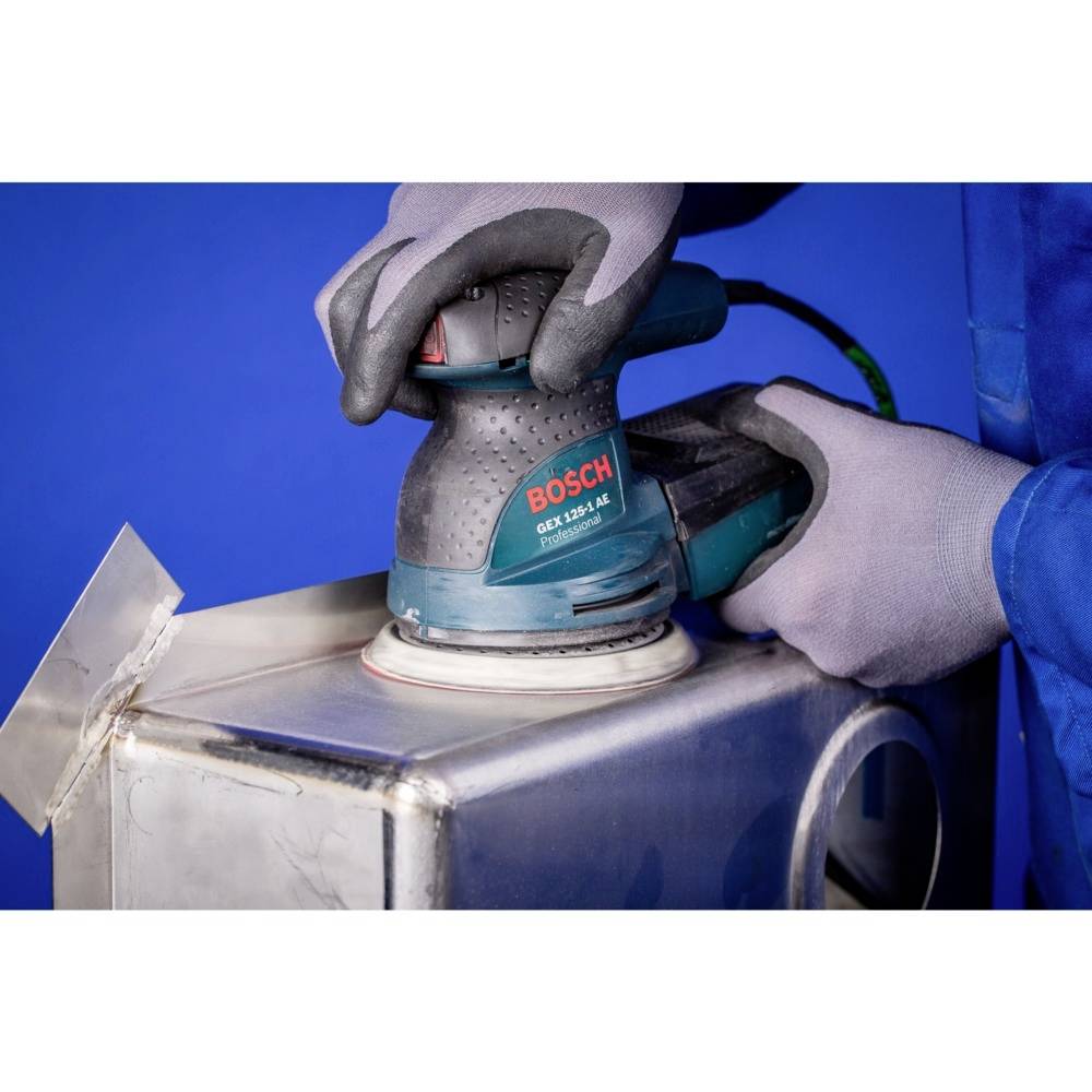 Osoba szlifuje powierzchnię metalową za pomocą urządzenia Bosch, nosząc rękawice ochronne. Jest skoncentrowana na wykonywanej czynności rzemieślniczej.