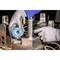 Osoba w szarych rękawiczkach używa drutu trasującego na metalowym elemencie w warsztacie. W tle widoczne są narzędzia i maszyny.