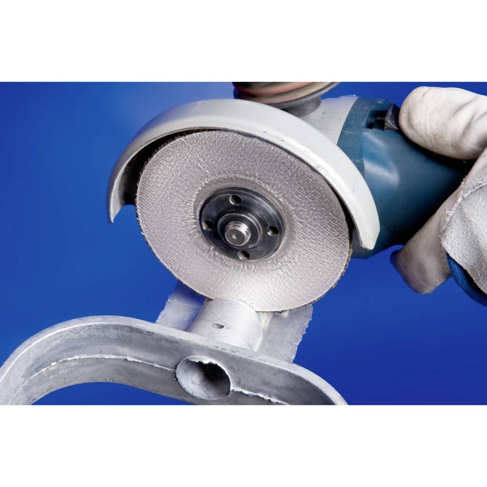 Zbliżenie pracującej szlifierki kątowej obrabiającej metal. Niebieskie tło. Ręka trzymająca urządzenie.