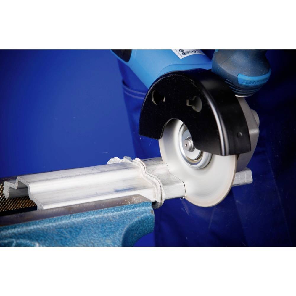 Szlifierka kątowa przecina kawałek metalu zamocowany w niebieskich imadłach. Tło również jest niebieskie.