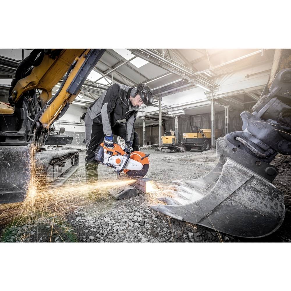 Robotnik w odzieży ochronnej przecina metalową powierzchnię wydajną piłą spalinową na placu budowy. Dookoła lecą iskry.