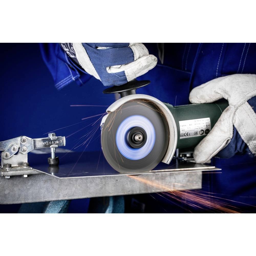 Osoba przecina metal szlifierką kątową. Od tarczy szlifierskiej odlatują iskry. Pracownik jest ubrany w odzież ochronną i rękawice.