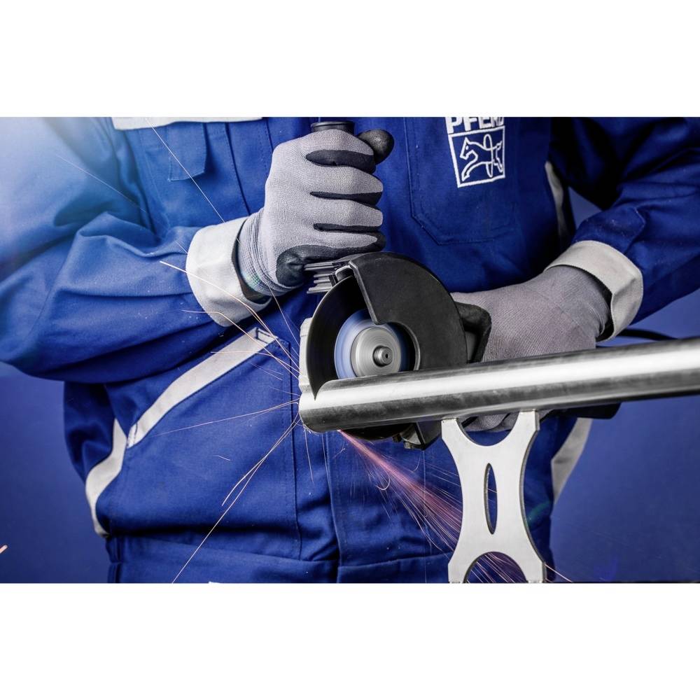 Osoba w odzieży ochronnej szlifuje rurę metalową szlifierką kątową. Tryskają iskry, niebieskie tło ściany.