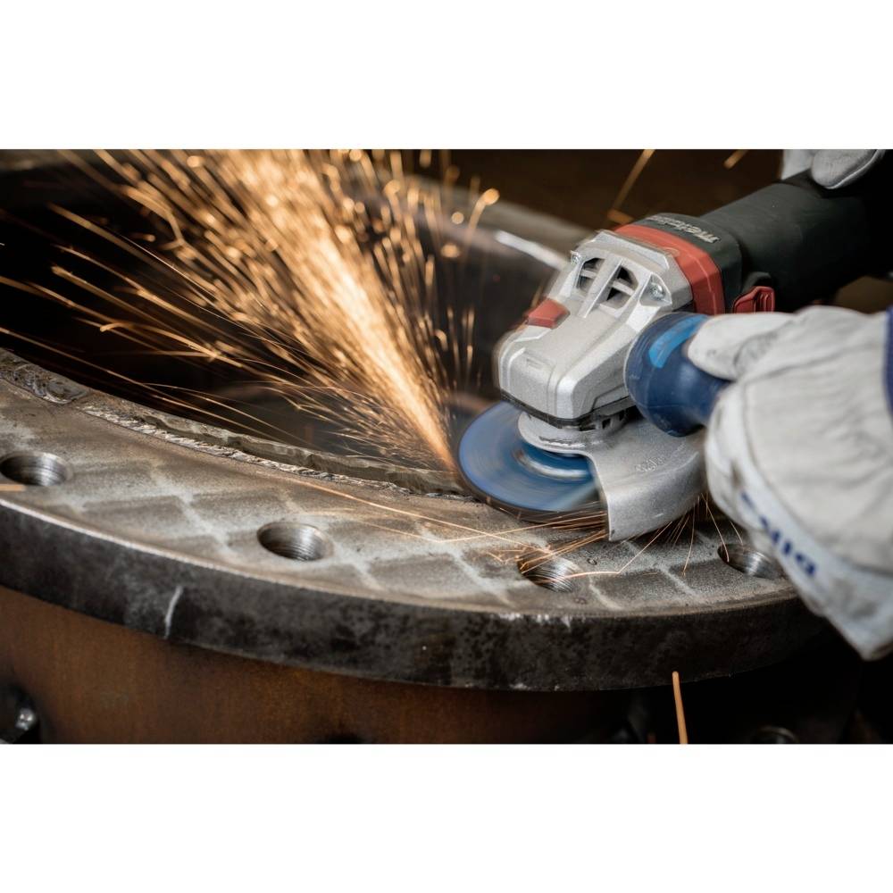 Osoba szlifuje metal kątnówką, lecą iskry. Odzież ochronna chroni ręce.