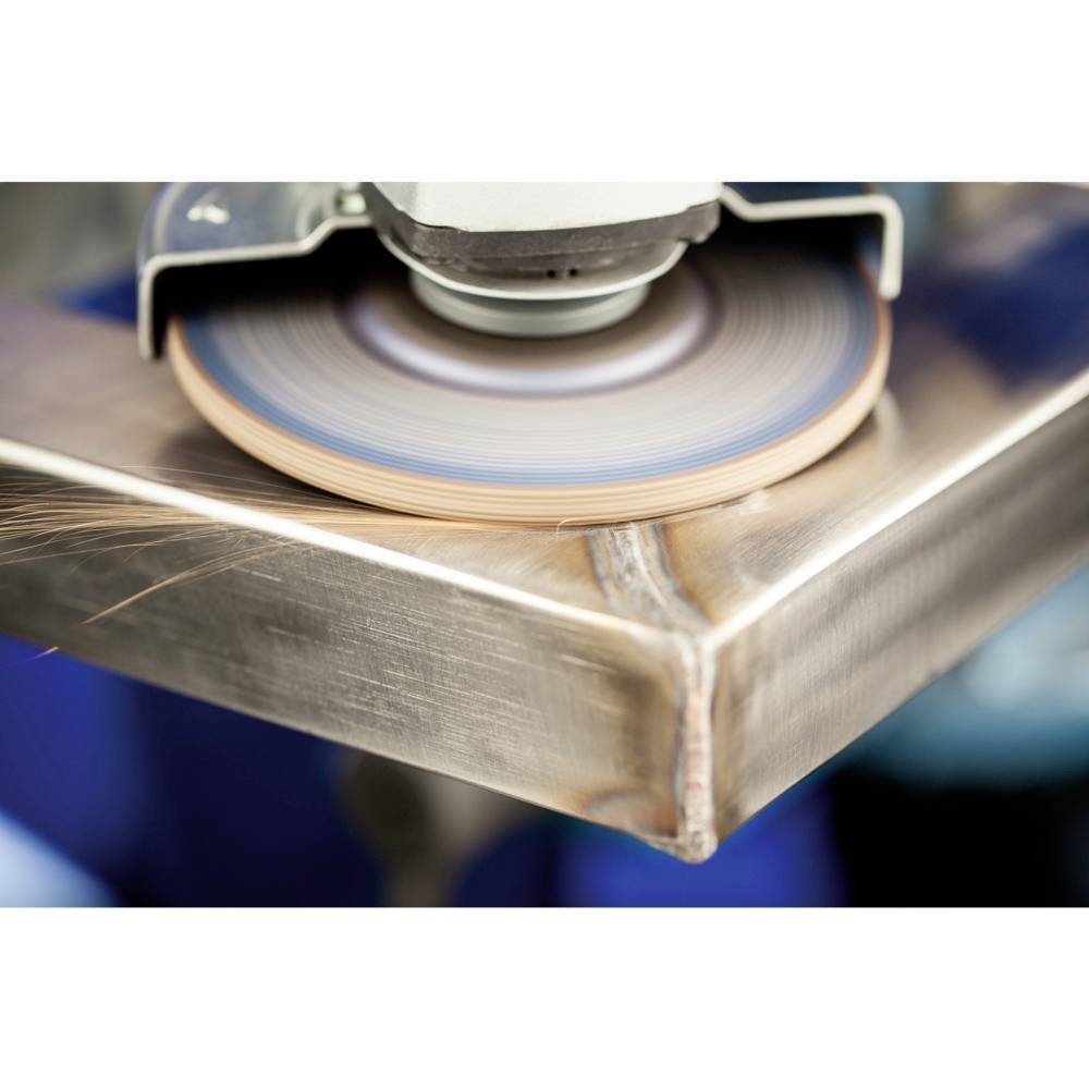 Zbliżenie kątnicy polerującej krawędź metalowej powierzchni; w rogu zdjęcia widać lecące iskry.