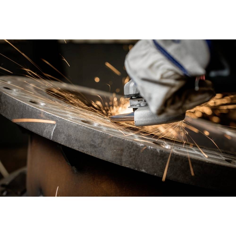 Osoba szlifuje metal za pomocą szlifierki kątowej, przez powietrze lecą iskry. Nosi odzież ochronną.