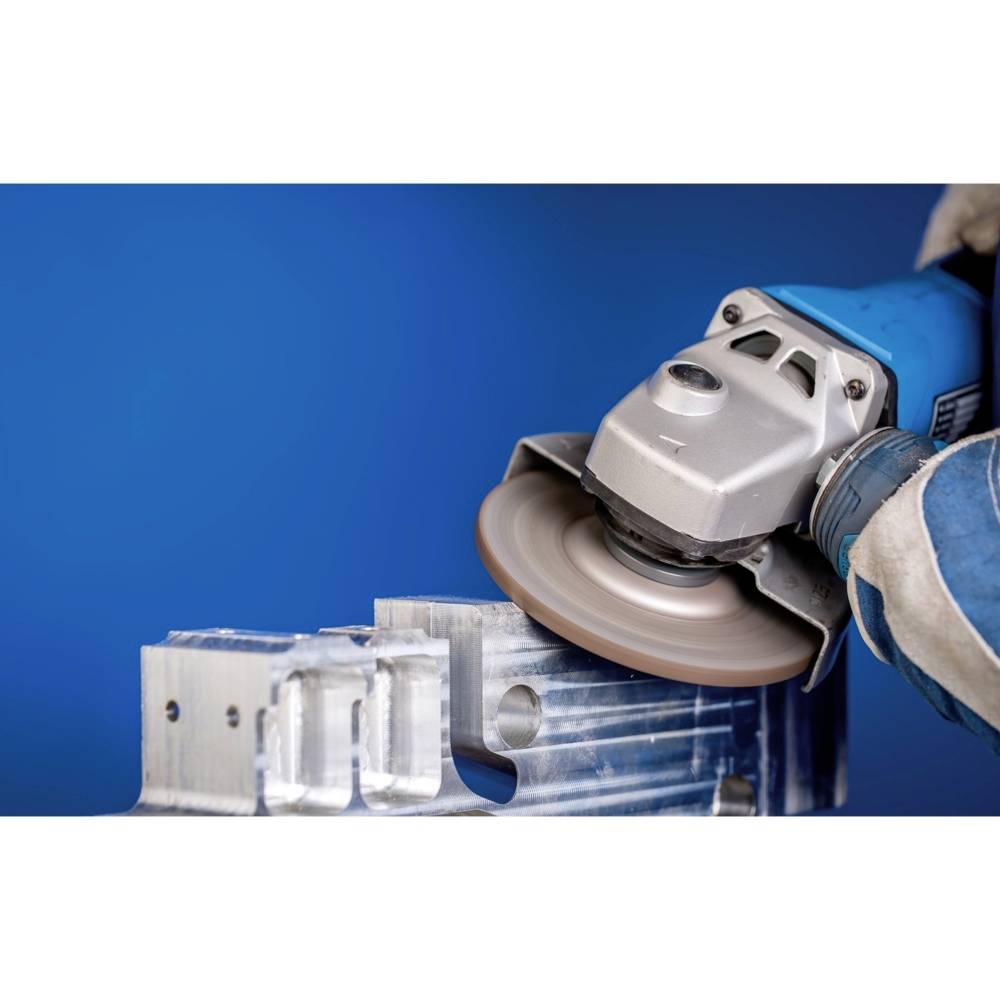 Osoba szlifuje powierzchnię metalową szlifierką kątową, widoczny niebieski tło i rękawica.