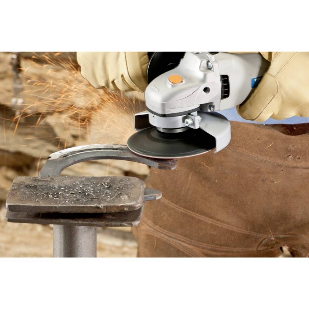 Osoba w rękawicach szlifuje metal szlifierką kątową, a dookoła lecą iskry. W tle widoczne są deski drewniane.