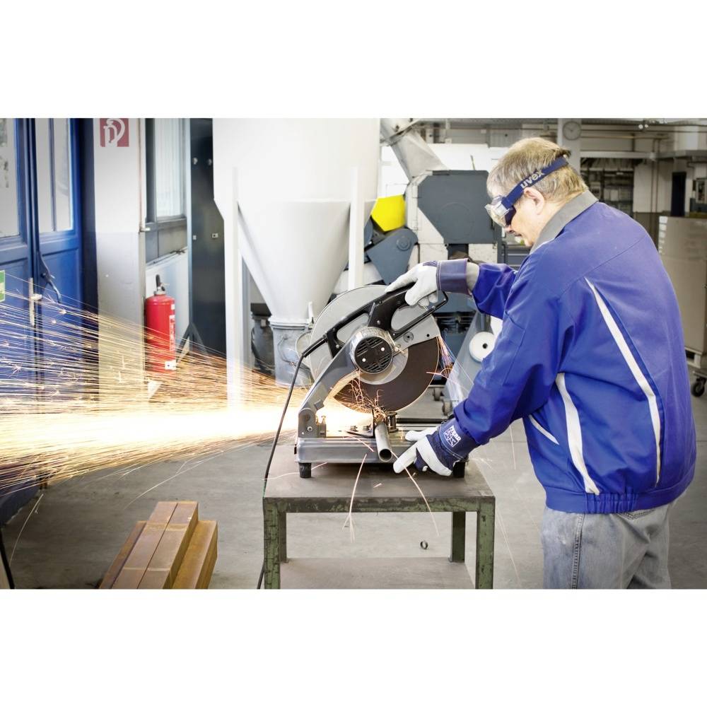 Mężczyzna w niebieskim ubraniu roboczym tnie metal tarczą tnącą. Iskry rozbryzgują się na boki. Ma na sobie okulary ochronne i rękawice.
